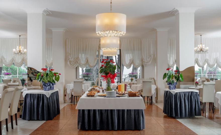 Elegant restaurant with set tables and floral decorations, illuminated by large chandeliers.